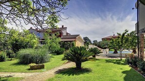 A well-maintained garden with a paved pathway, various plants, and a pool area. - Apartment with pool and only 700 meters to sandy beach (Medulin)