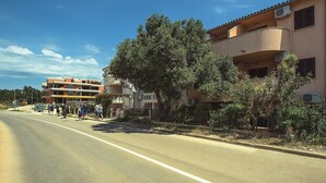 A multi-story building with balconies, a clear sky, and a road with pedestrians. - Only 100 meters to beach in Medulin with air conditioning, WiFi (Medulin)