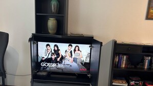A living room with a TV on a stand, a bookshelf, and a wooden floor.