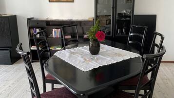 A dining area with a black table, red cushioned chairs, a vase with flowers, and a bookshelf in the background.