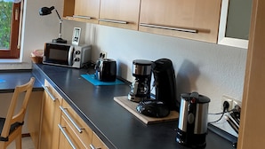 A compact kitchen with wooden cabinets, a black countertop, a toaster, a coffee maker, and a kettle.