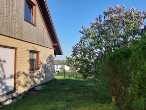 A two-story wooden house with a brick facade, a small front yard, and a flowering tree.