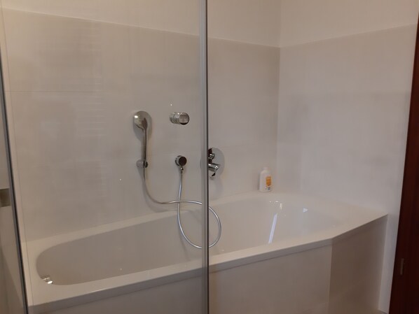A modern bathroom with a glass-enclosed shower, a white bathtub, and a small bottle of shampoo on the wall.