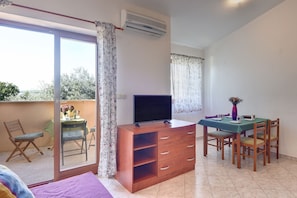 Una habitación con televisión, una mesa de comedor con sillas, un balcón con una silla y un patio corredero.