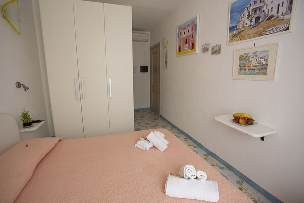 A hotel room with a bed, a wardrobe, a shelf with fruits, and artwork on the walls. - Celestina (Lacco Ameno)