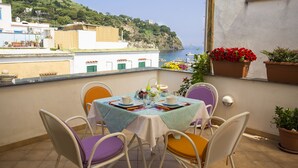 Una terraza con una mesa dispuesta para dos personas, con vistas a la costa, edificios y una colina.