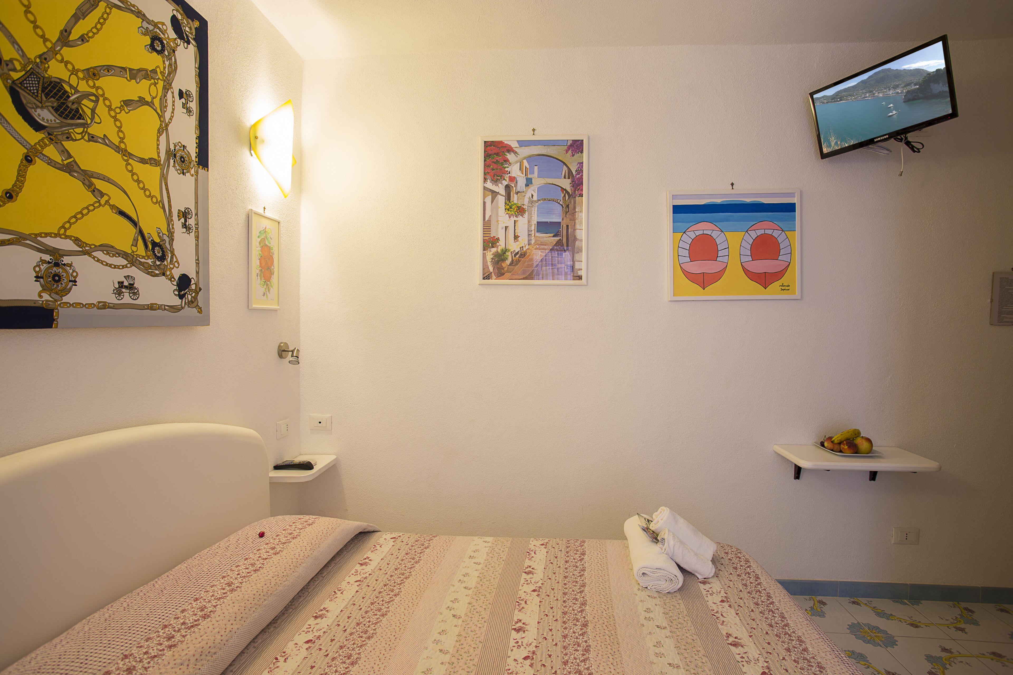 A hotel room with a bed, a small bedside table, a wall-mounted TV, and artwork.