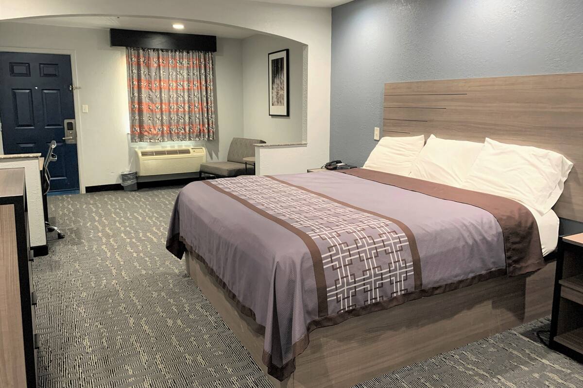A hotel room with a bed, a desk, a chair, a picture on the wall, and a door.