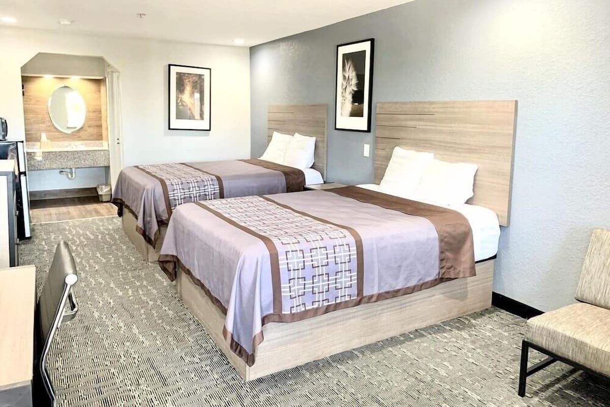 A hotel room with two beds, a desk, a chair, and a bathroom.