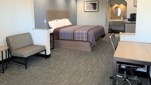 Een compacte hotelkamer met een bed, een klein bureau, een stoel en een kitchenette.