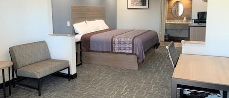Ein kompaktes Hotelzimmer mit Bett, kleinem Schreibtisch, Stuhl und einer Küchenzeile.
