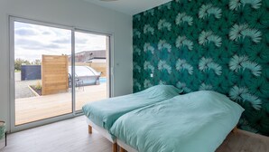 A bedroom with a bed, a sliding glass door leading to an outdoor area, and a wall with a leaf pattern. - VILLA SAINT ANTOINE - 9 people (Plouescat)