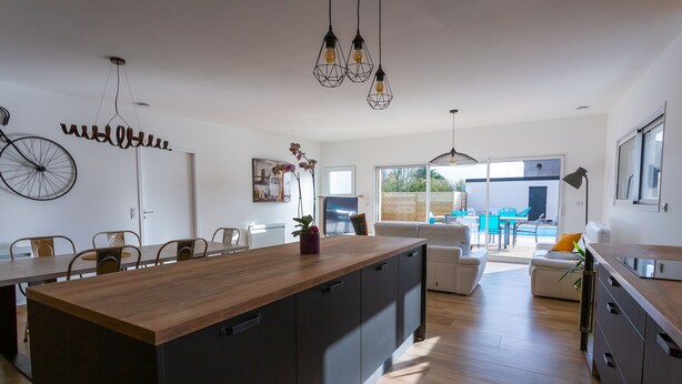 A modern kitchen with a central island, dining area with chairs, and a view to the outside. - VILLA SAINT ANTOINE - 9 people (Plouescat)