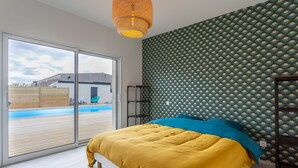 A bedroom with a large bed, a view of a swimming pool through a sliding door, and a patterned wallpaper. - VILLA SAINT ANTOINE - 9 people (Plouescat)