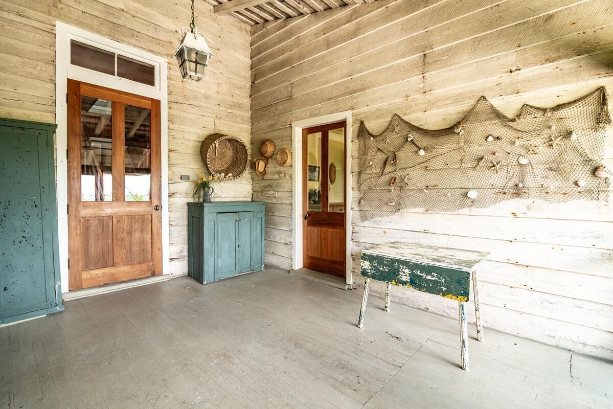 Une pièce rustique aux murs et à la porte en bois, avec un meuble bleu et une table ornée d’un filet décoratif accroché au mur.