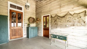 Habitació rústica amb parets de fusta, una porta de fusta, un armari blau i una taula amb una xarxa decorativa a la paret.