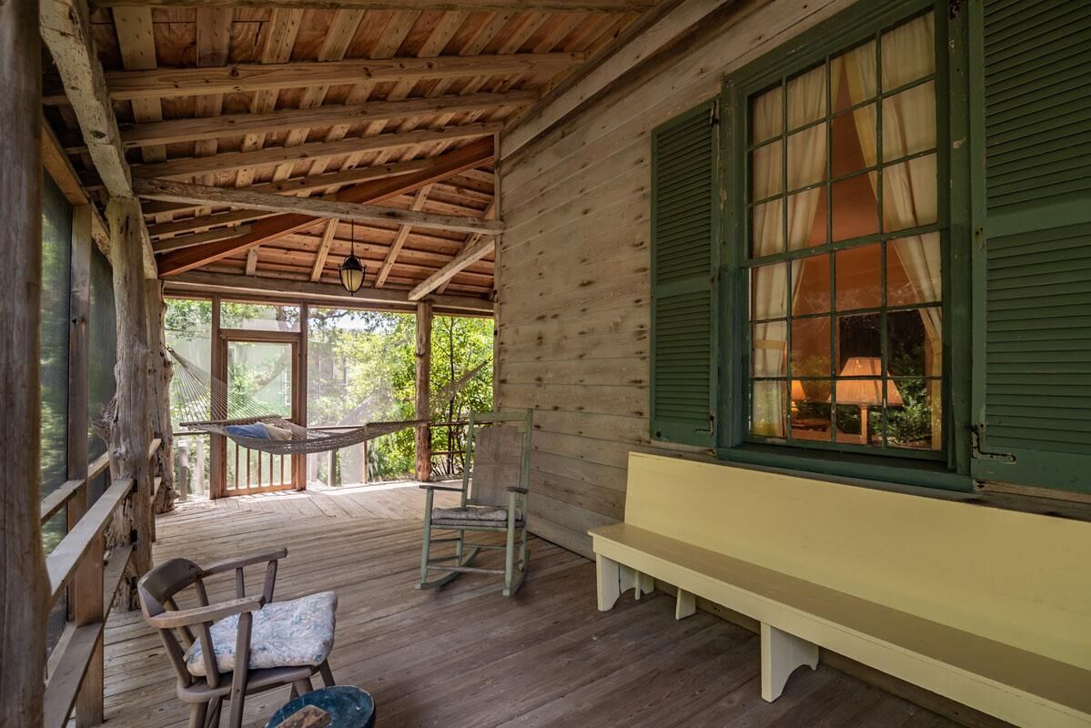 Een houten chalet met een veranda, een hangmat, een bank en een raam met gordijnen.
