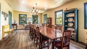 Una sala menjador amb taula i cadires de fusta, un penjallum i una estantàcia plena de plats.