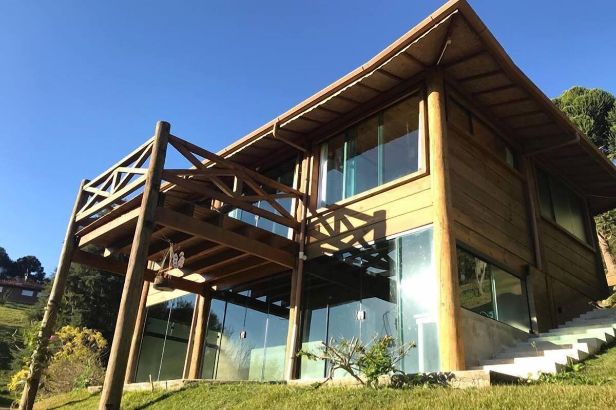 Une maison moderne en bois, dotée de grandes fenêtres en verre et d’une terrasse en bois.