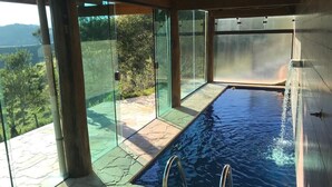 A modern indoor swimming pool with glass walls, a stone floor, and a view of the outdoors. - Jardim Suspenso da Babilônia (Santo Antonio do Pinhal)