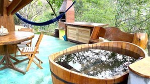 A wooden hot tub with a wooden table and chairs nearby, surrounded by greenery. - Jardim Suspenso da Babilônia (Santo Antonio do Pinhal)