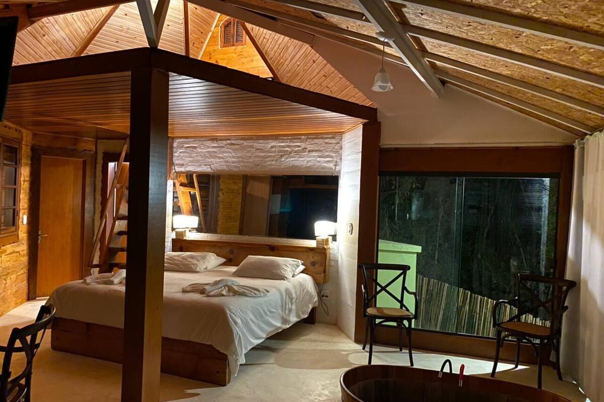 Une chambre confortable avec un plafond en bois, un grand lit, un coin salon avec une baignoire et une vue dégagée sur l’extérieur grâce à une grande fenêtre.