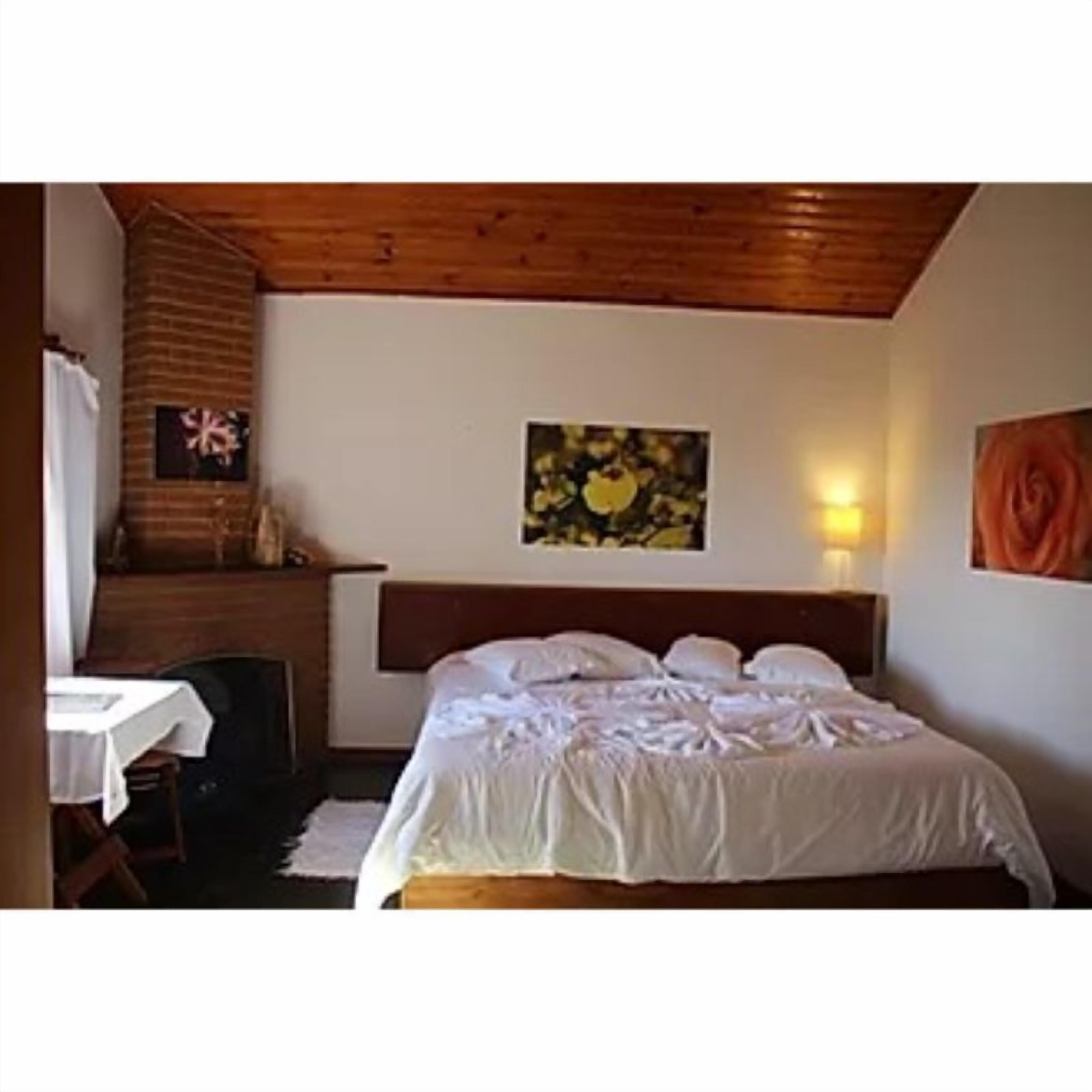 A bedroom with a wooden headboard, a bed with white bedding, a small table with a white tablecloth, and a wall-mounted picture.