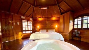 A wooden cabin with a large bed, a hot tub, and a window with a view. - Jardim Suspenso da Babilônia (Santo Antonio do Pinhal)