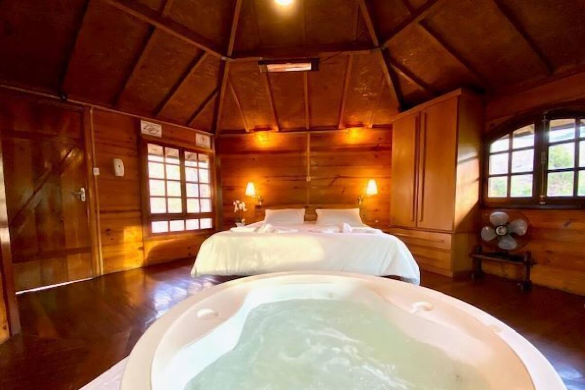 Une cabane en bois avec un grand lit, un jacuzzi et une fenêtre donnant sur un paysage magnifique.