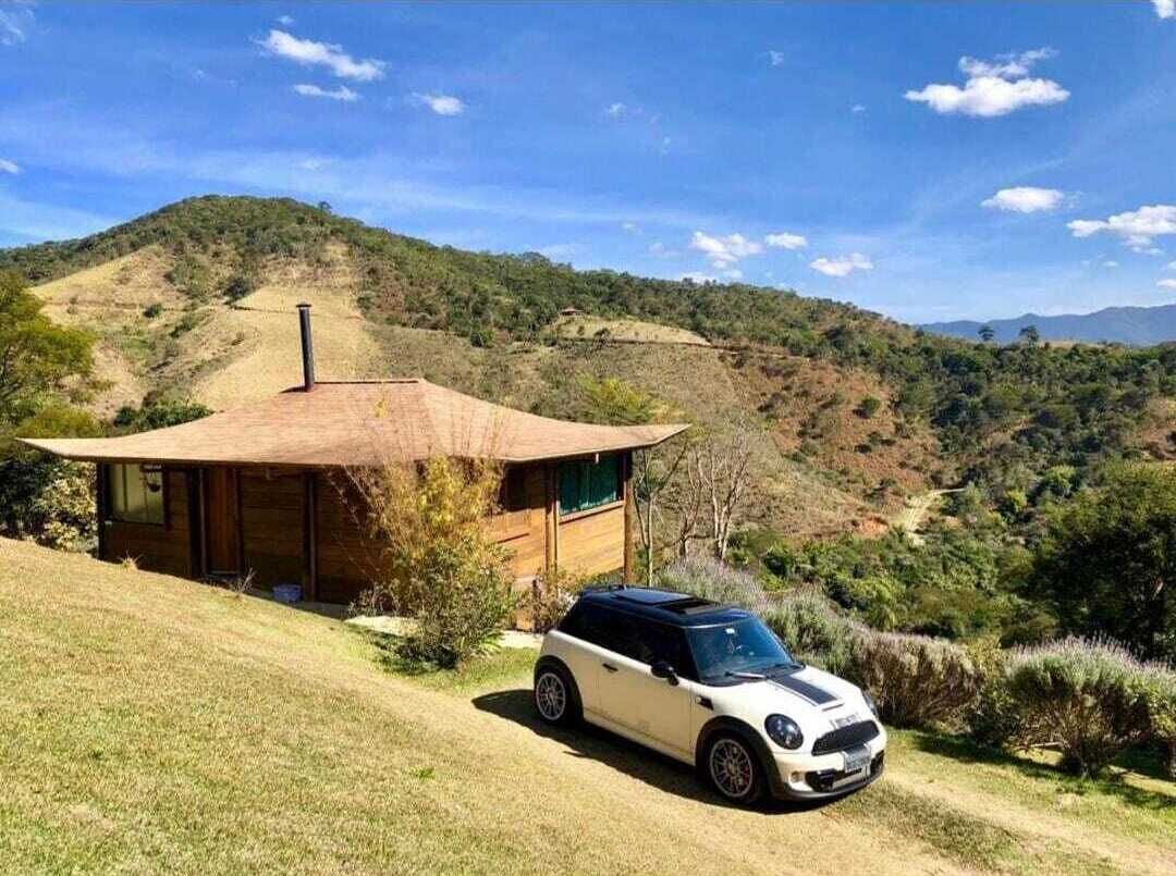 Un Mini Cooper blanco estacionado frente a una cabaña de techo inclinado, en un paisaje montañoso.