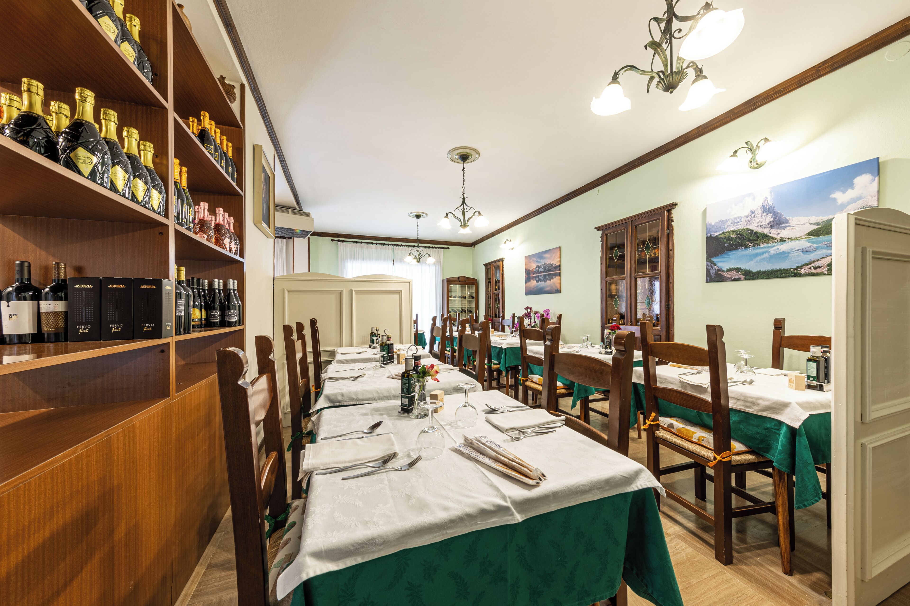 Un comedor con mesas largas, sillas y una estantería para vinos con botellas.