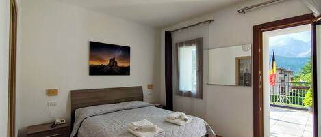 A bedroom with a bed, a bedside table, a painting, a window, and a view of the outside.