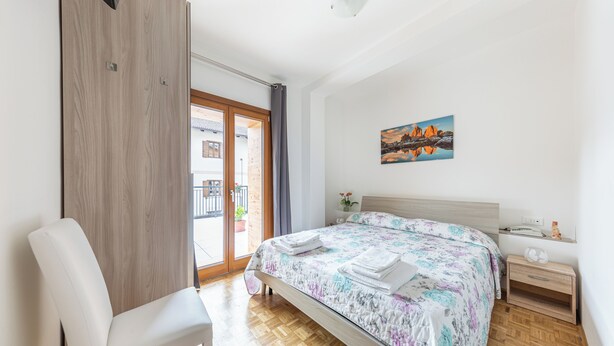 A bedroom with a bed, a chair, a wooden wardrobe, a nightstand, and a painting on the wall. - Hotel da Marco (Vigo di Cadore)