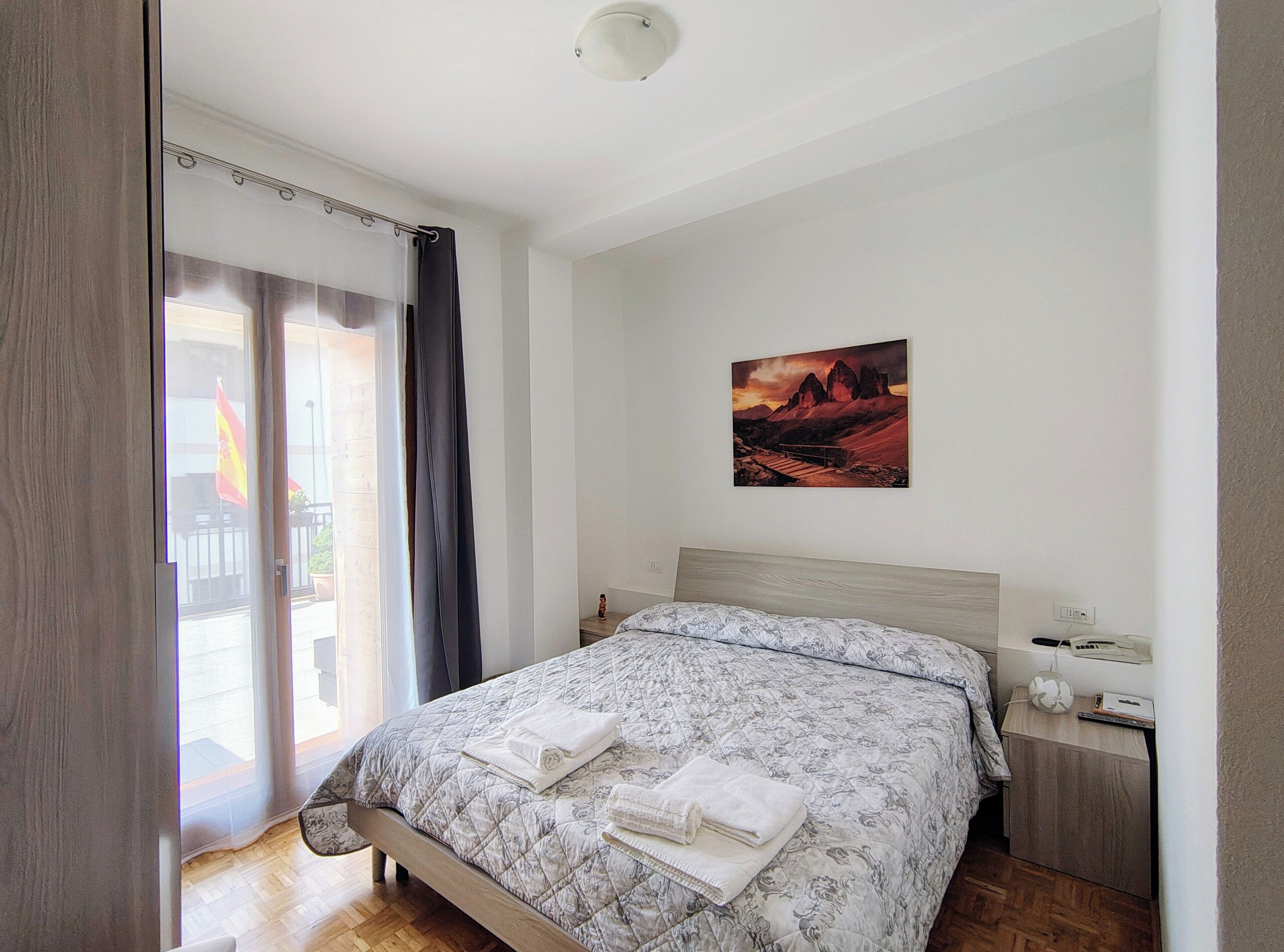 Un dormitorio con cama, mesita de noche, un cuadro colgado en la pared y una puerta corrediza de vidrio que da a un espacio exterior.