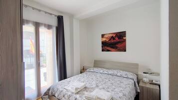 Un dormitorio con cama, mesita de noche, un cuadro colgado en la pared y una puerta corrediza de vidrio que da a un espacio exterior.