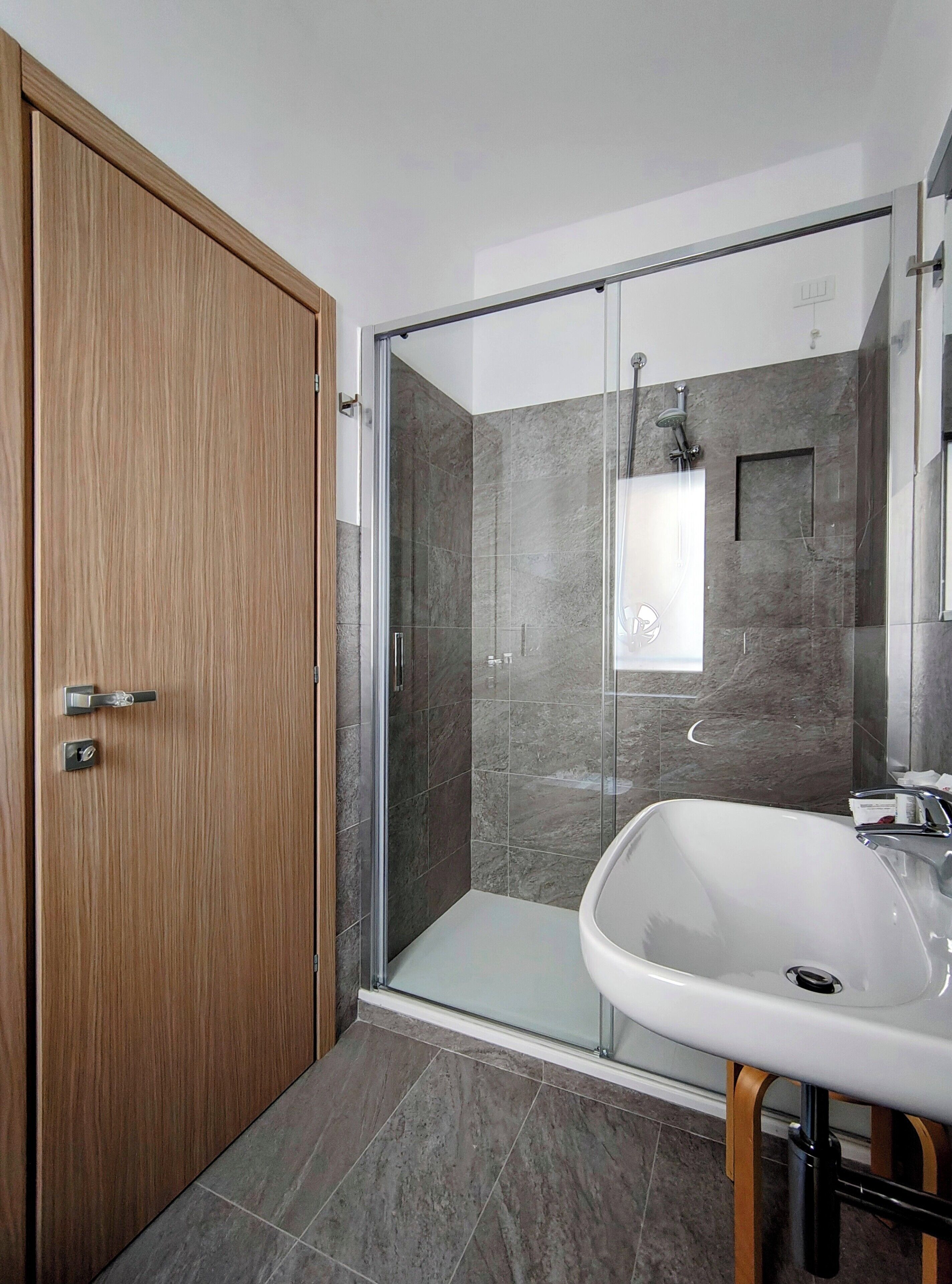 Ein modernes Badezimmer mit Holztür, Duschkabine aus Glas und Waschbecken in Weiß.