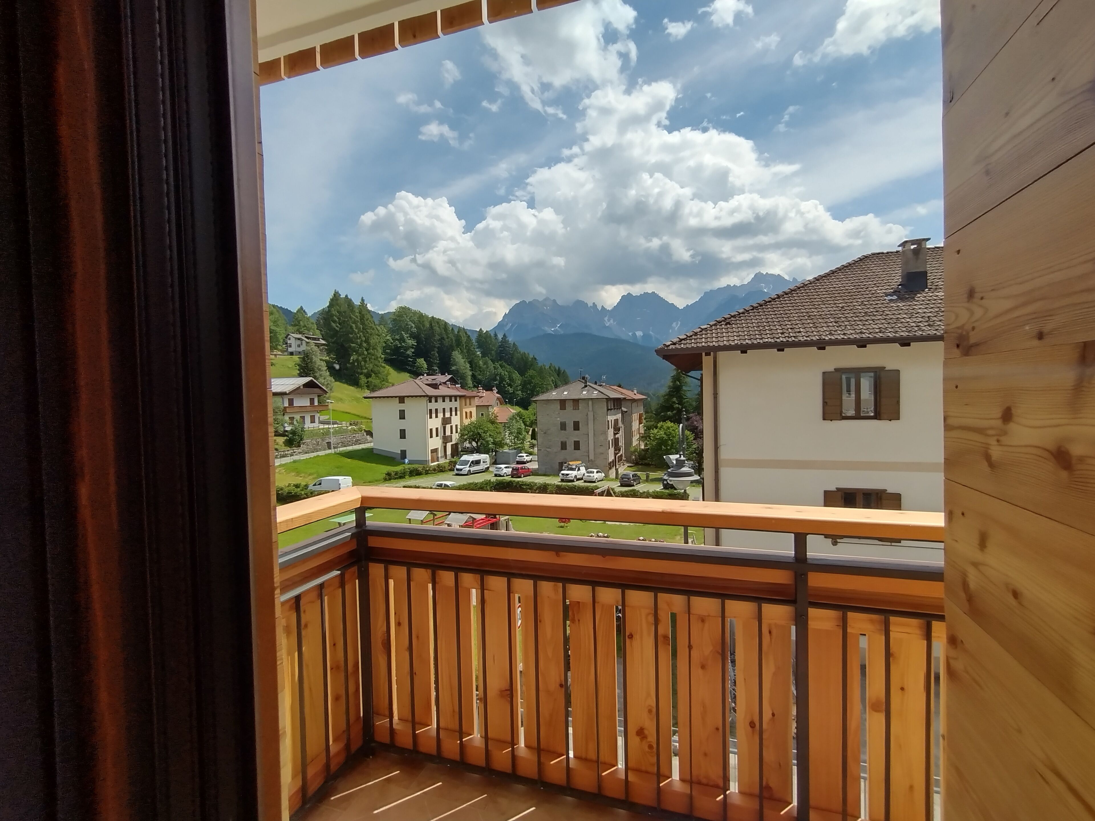 A balcony with a wooden railing overlooking a residential area with houses and mountains in the background.