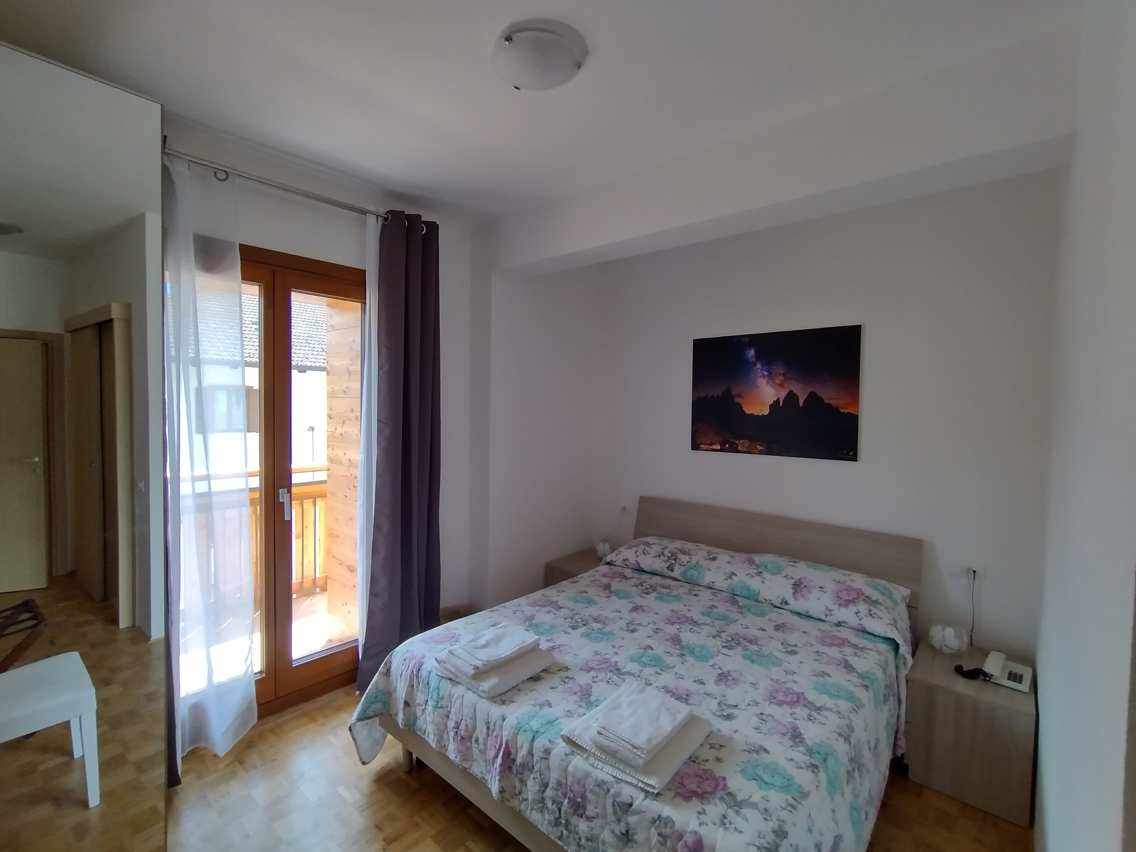 Una camera da letto con un letto, un comodino con il telefono, una finestra con tende e un quadro al muro.