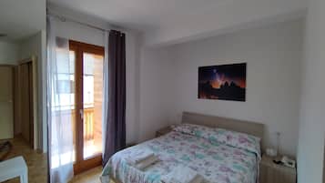 Una camera da letto con un letto, un comodino con il telefono, una finestra con tende e un quadro al muro.