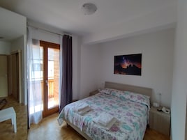 Un dormitorio con una cama, una mesita de noche con un teléfono, una ventana con cortinas y un cuadro en la pared.