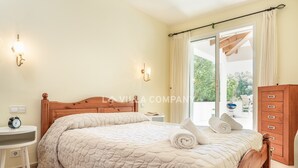 A bedroom with a wooden bed, a bedside table with a lamp, and a view of the outdoors through a sliding glass door. - Wonderful villa with country views, private pool, sleeps 6, AC (Binixica)