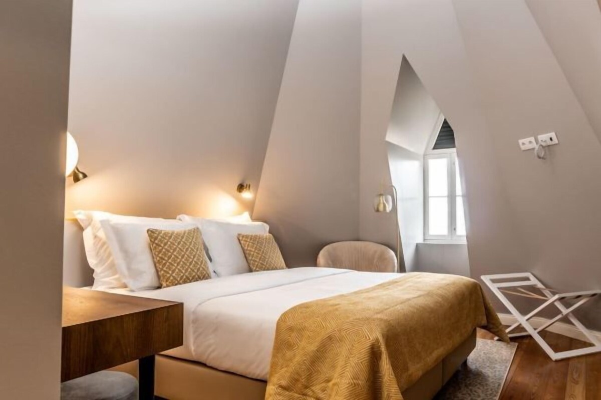Un dormitorio con cama, mesitas de noche, una silla y una ventana.