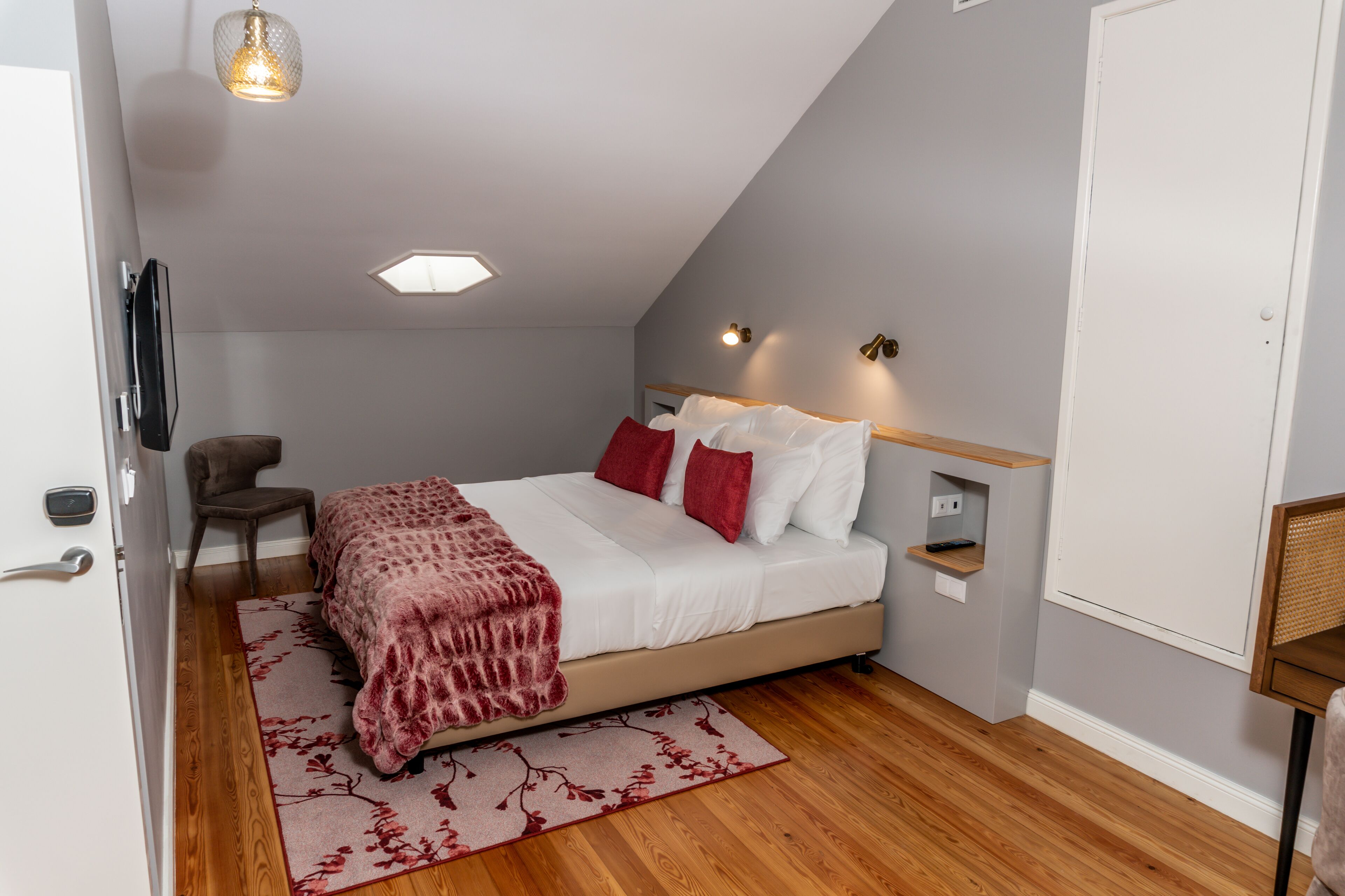 A bedroom with a bed, a chair, a desk, and a TV.