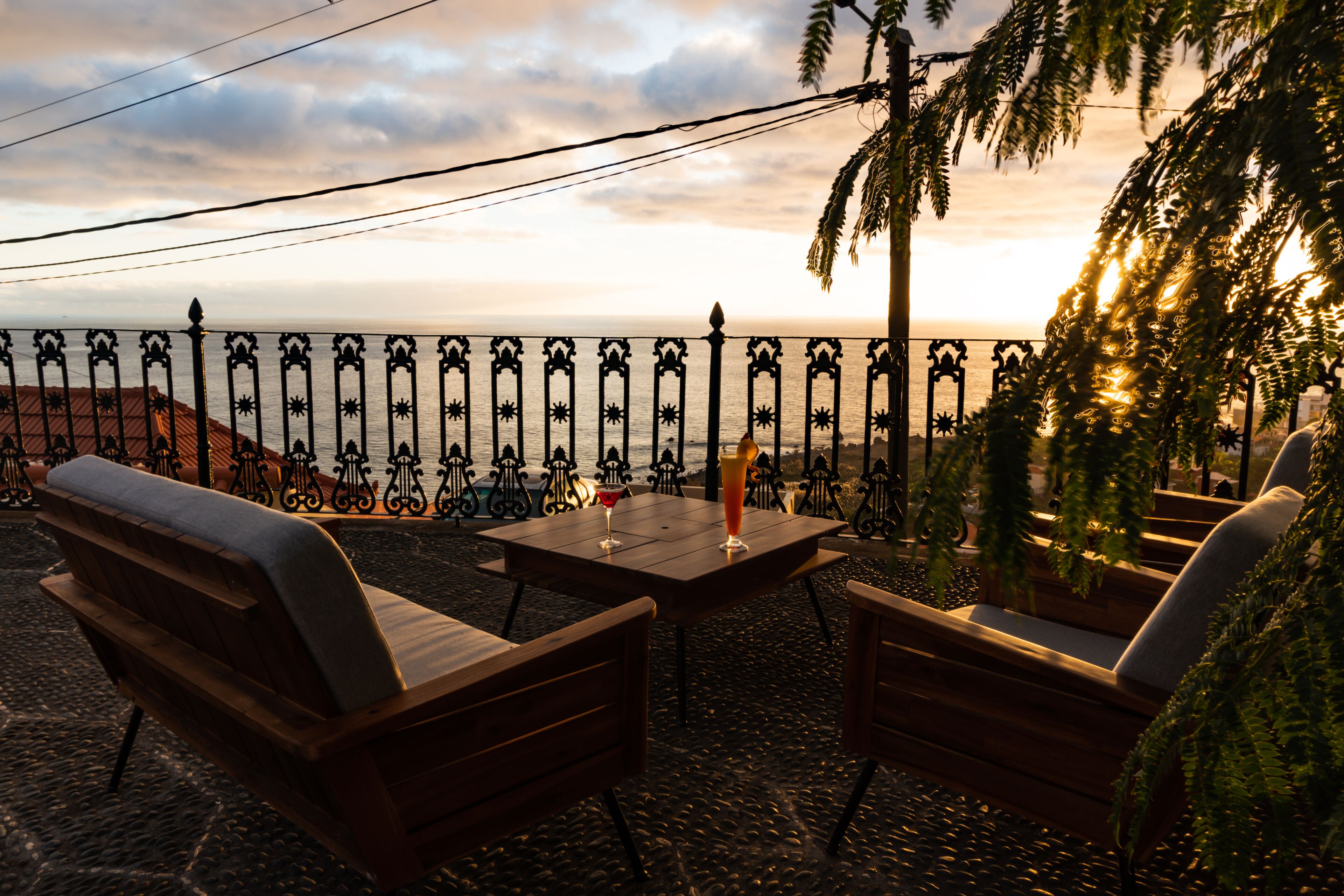 A terrace with wooden furniture and a view of the sea at sunset.