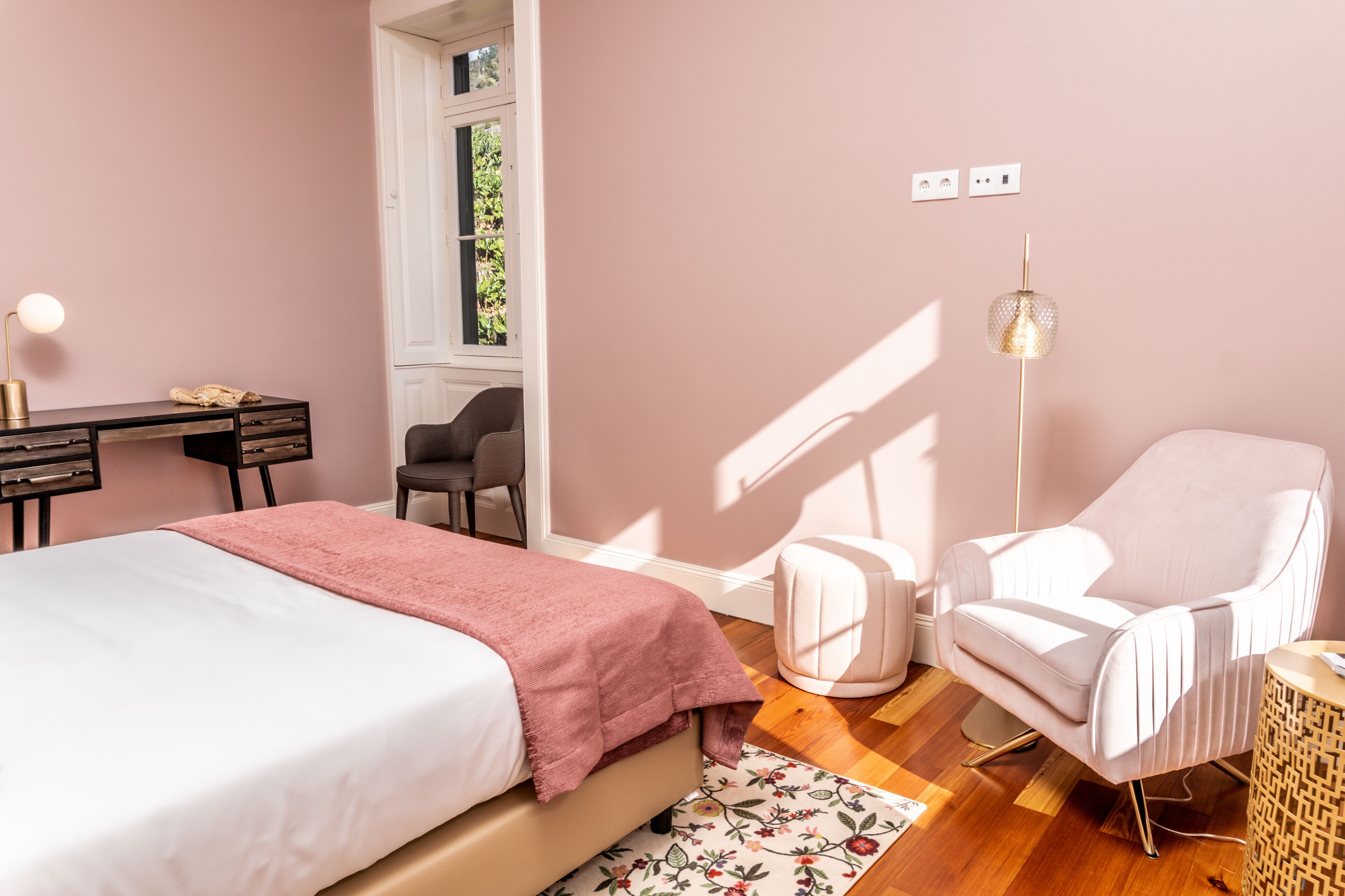 A bedroom with a bed, a desk, a chair, a floor lamp, and a window.
