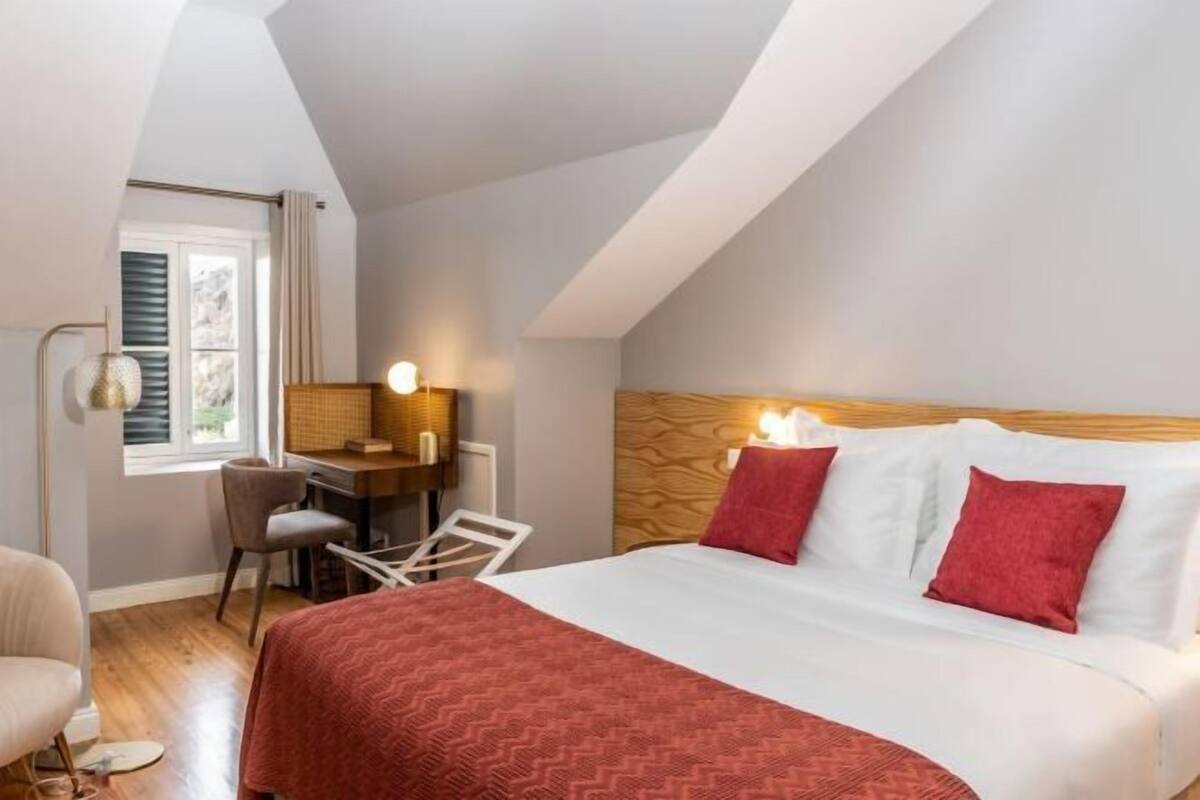 A bedroom with a bed, a desk, a chair, and a window.