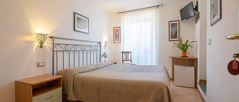 Un dormitorio con cama, mesita de noche, lámpara, televisor y un escritorio pequeño con una planta.