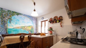 A kitchen with a dining area, a painting on the wall, a stove, and a coffee maker. - B&B Il Vigneto in the heart of the Cinque Terre (Volastra)