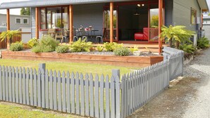 Een modern huis met een overdekt terras, houten terras en een omheinde tuin.