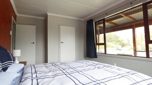 Een slaapkamer met een groot bed, twee deuren, een raam met gordijnen en een plafondlamp.